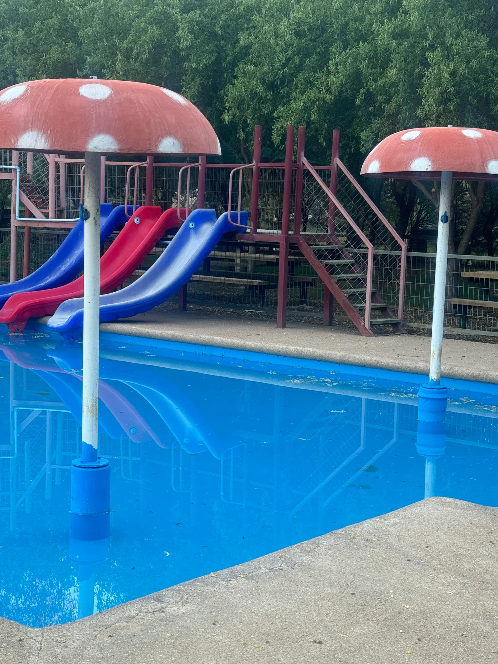 Tres canales de tobogán rojos y azules junto a las fuentes de hongos de la piscina infantil